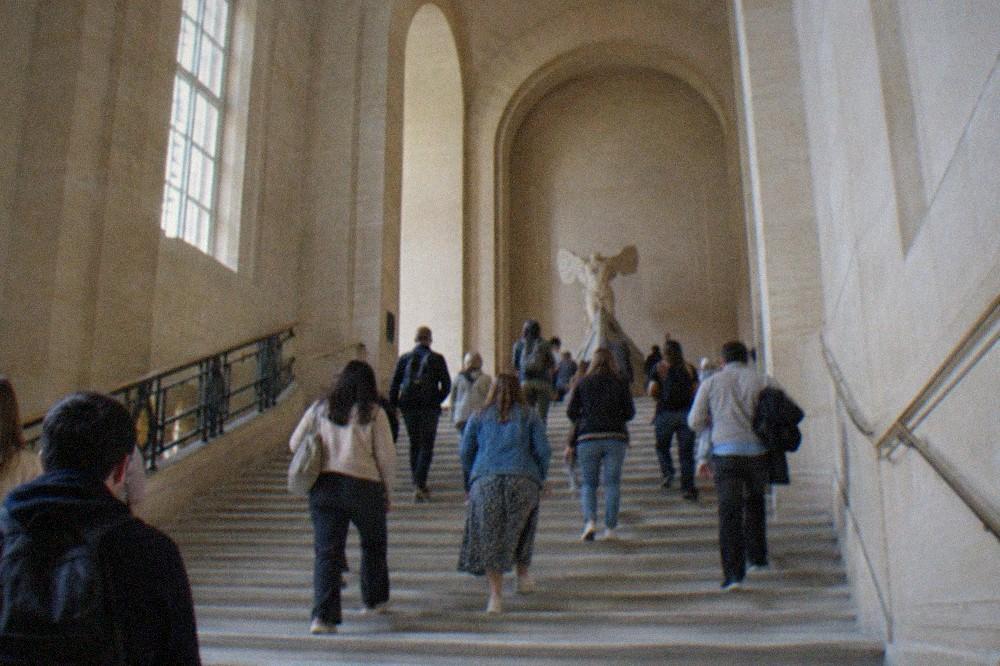 A wide stone staircase inside the Louvre crowded with visitors in casual clothing