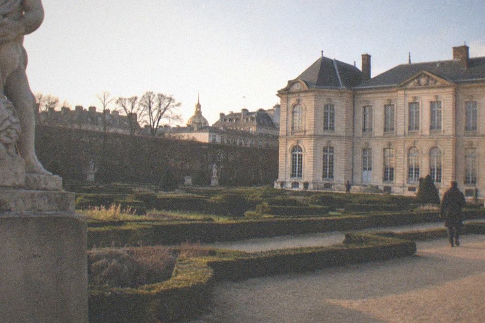 A formal garden with clipped hedges and sculptures in front of a classical mansion