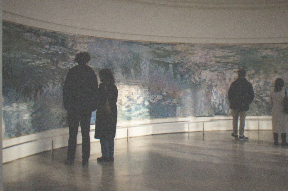 Visitors standing quietly in an oval gallery before wide curved water lily paintings