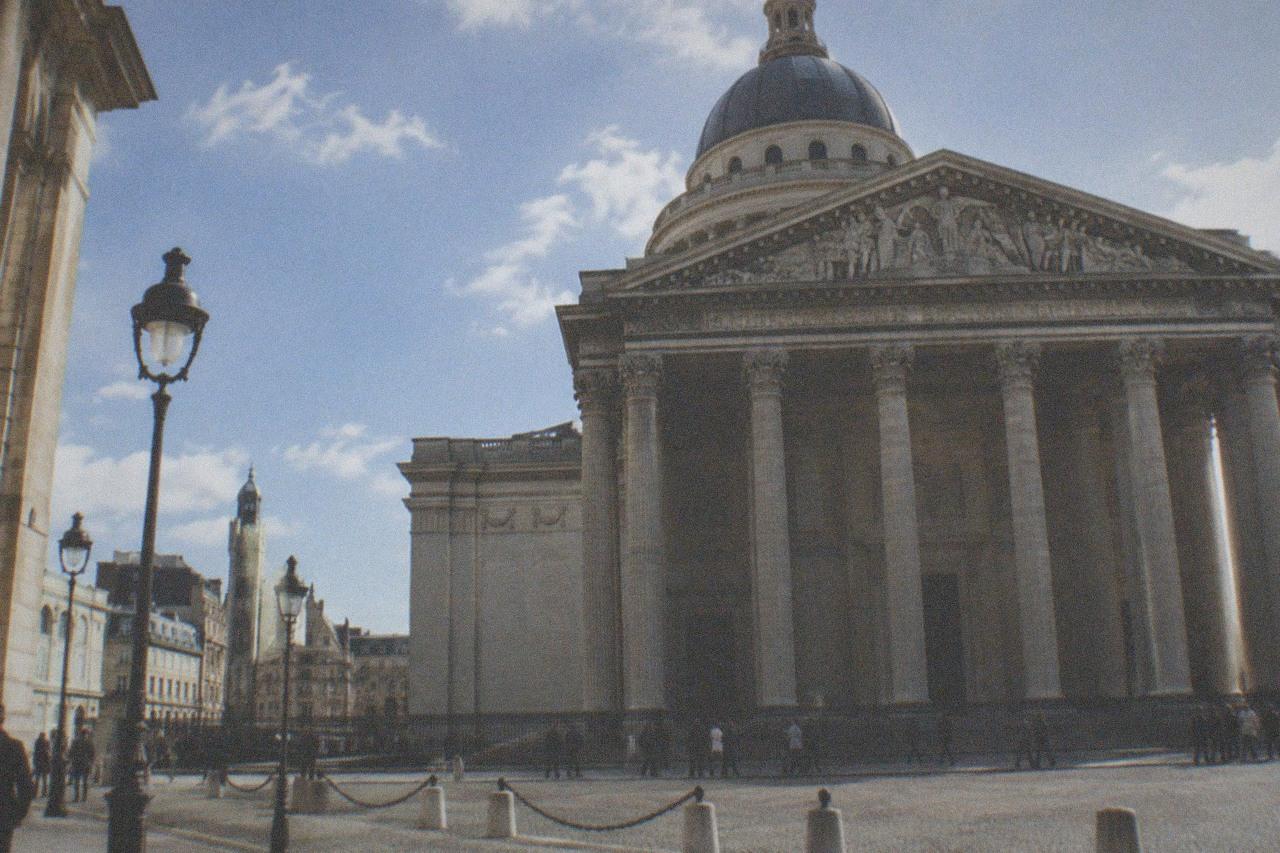 The Panthéon's neoclassical facade with its grand colonnade, seen from the Place du Panthéon on a sunny day.
