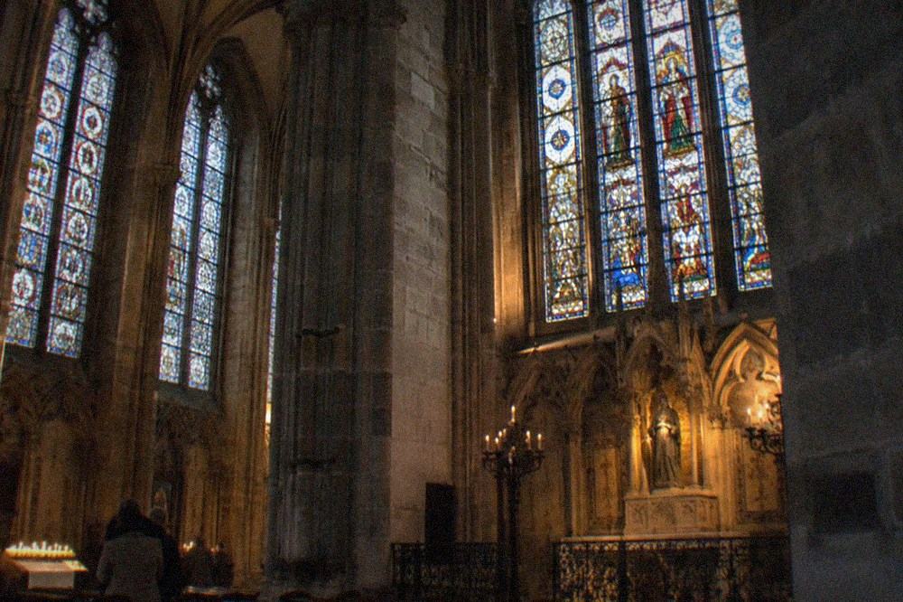 Tall medieval stained glass windows filling a stone chapel wall with colored light