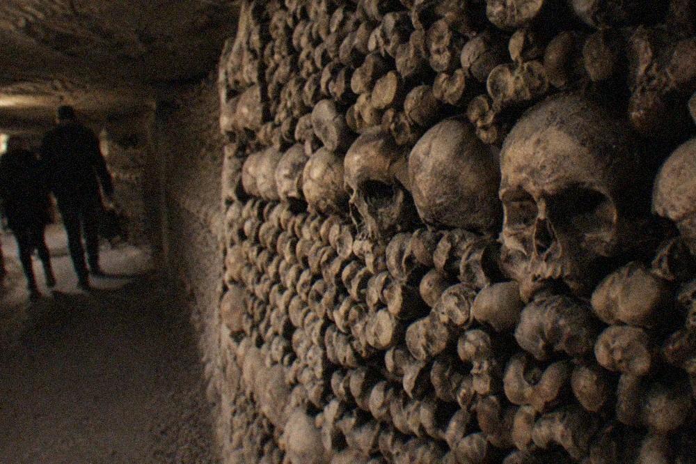 Tunnel wall of stacked skulls and long bones arranged in patterns underground
