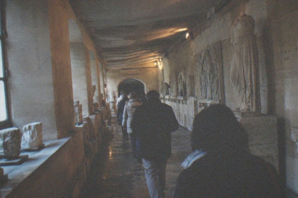 Visitors walking single file through a narrow low-ceilinged stone gallery lit by dim lamps
