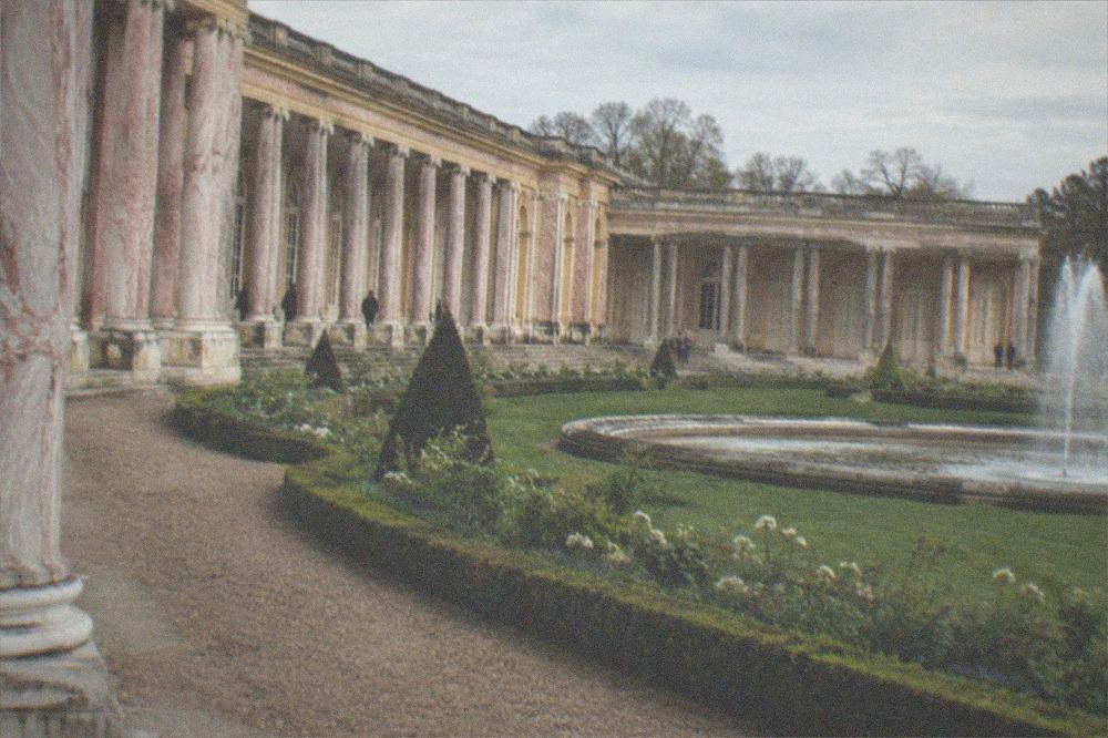 The Grand Trianon's pink marble colonnade with a formal garden and fountain in the foreground