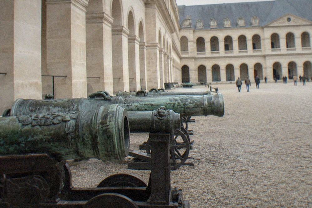 Rows of historical cannons and artillery pieces displayed along the gravel courtyard of Les Invalides