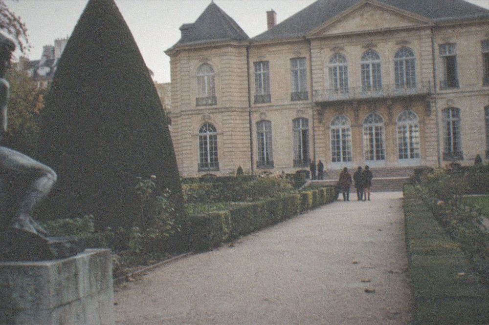 A gravel path in the Musée Rodin garden leading past a bronze statue toward the mansion facade