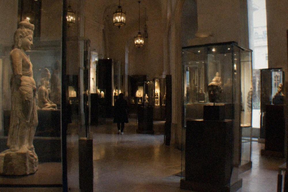 Gallery hall of the Musée Guimet with stone sculptures displayed in glass cases.