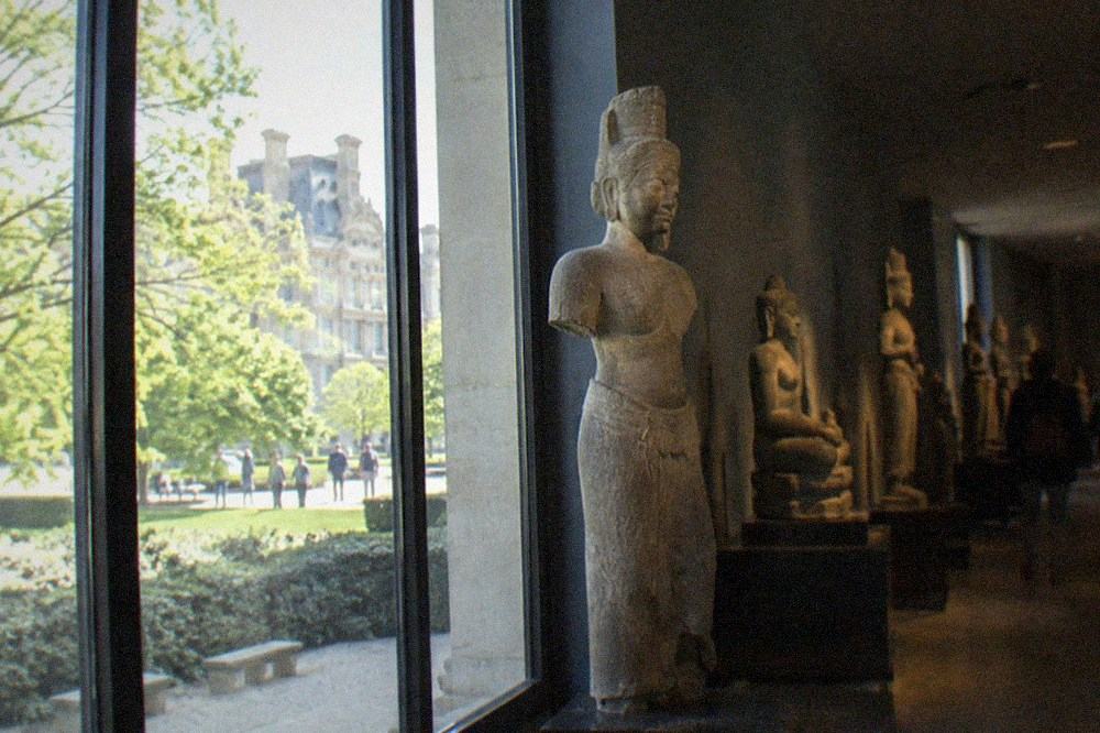 Dimly lit Cambodian sculpture gallery with stone figures arranged along a wall.