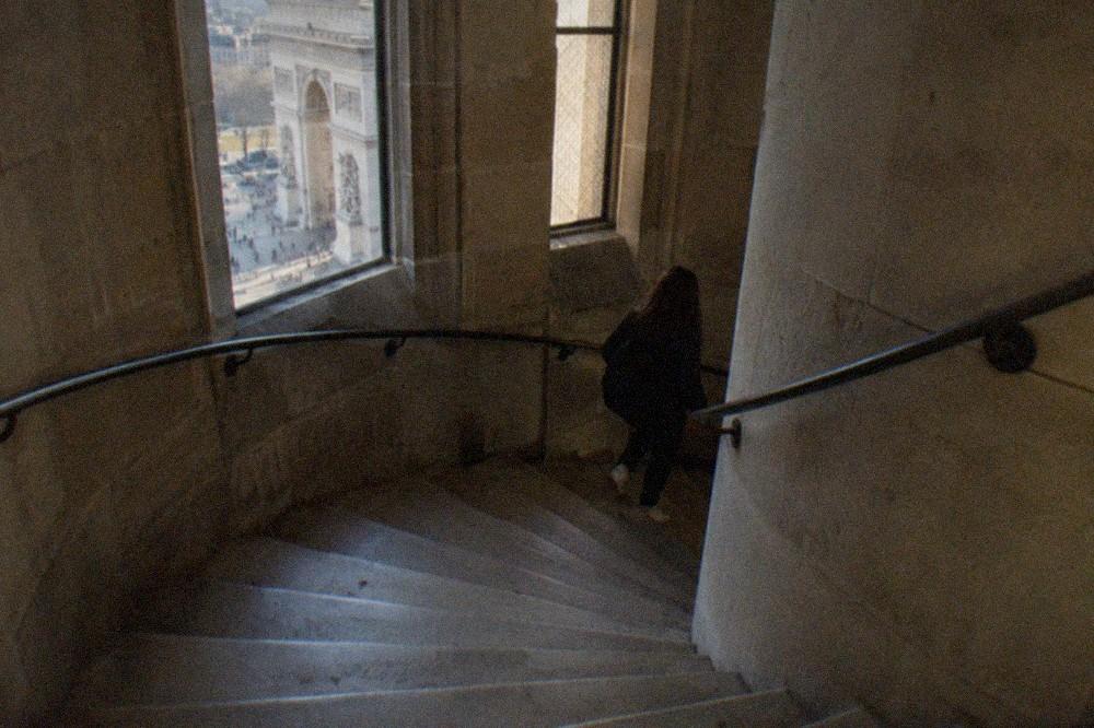 The spiral stone staircase inside the Arc de Triomphe winding upward past a landing
