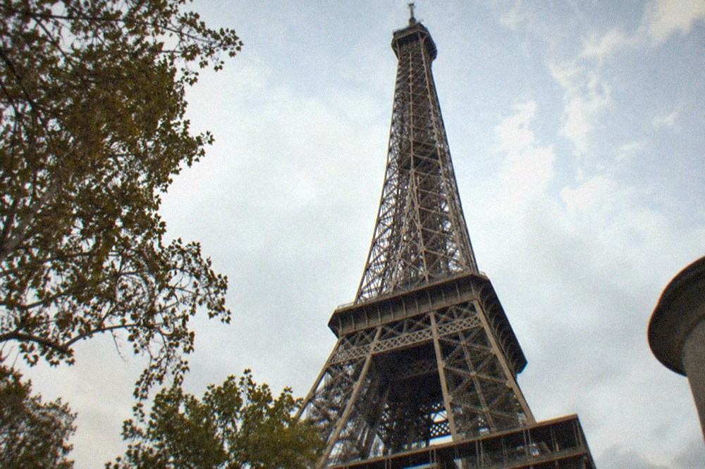 The summit of the Eiffel Tower seen from below, with the top platform and antenna narrowing against open sky.