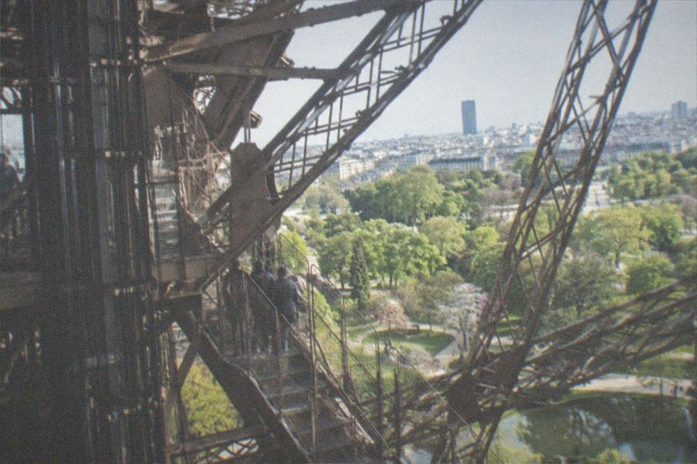 The Eiffel Tower's ironwork seen from the second floor, with lift machinery and stairways crossing the lattice structure.