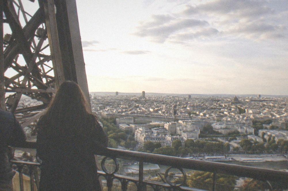 The city skyline spread out beyond the Eiffel Tower's upper structure, with rooftops fading toward the horizon under a wide sky.