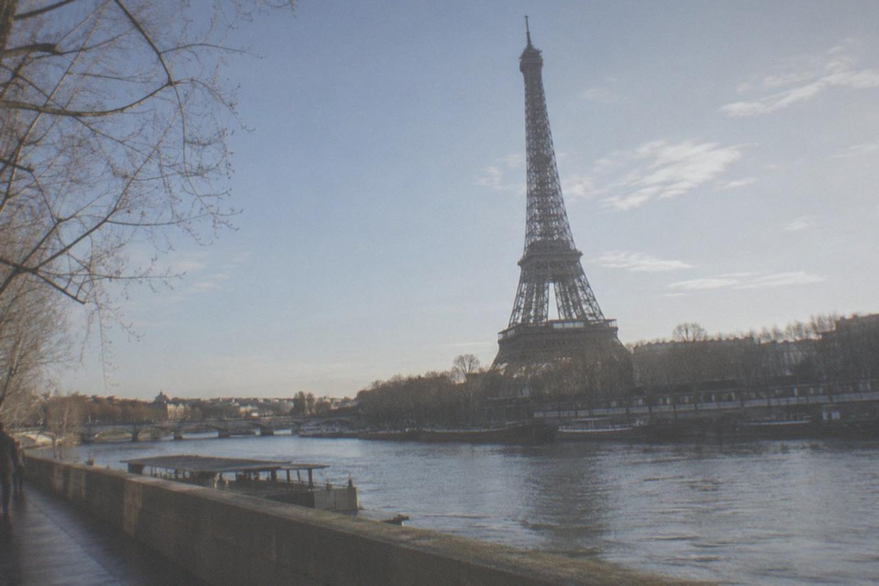 The Eiffel Tower rising above Paris rooftops on a clear afternoon, seen from across the Seine.