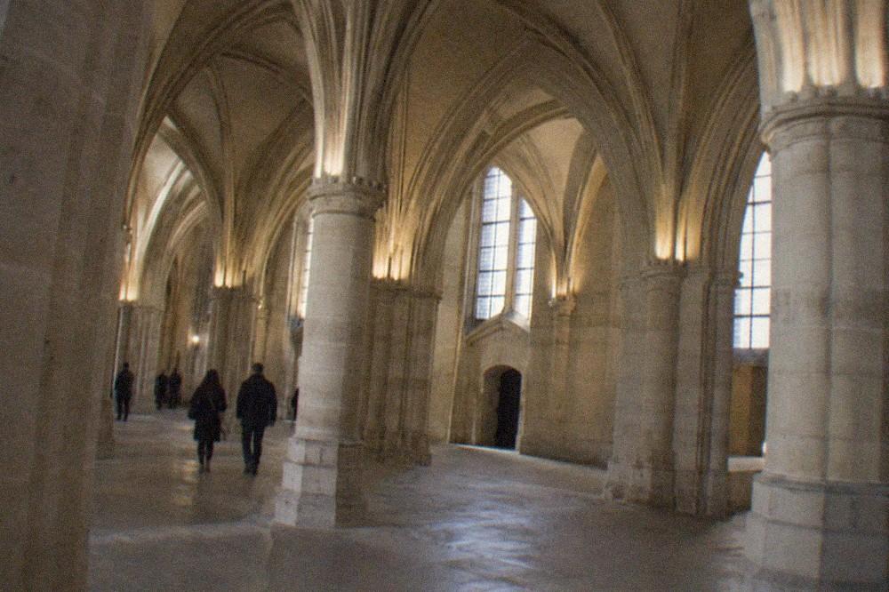 Vaulted Gothic hall of the Conciergerie with stone pillars and arched ceilings lit by high windows