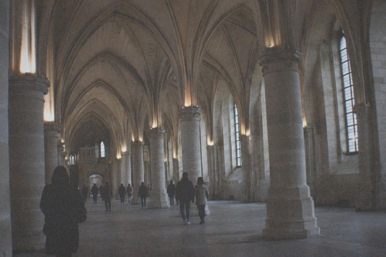 Gothic hall of the Conciergerie with vaulted stone arches and pillars lit by high windows