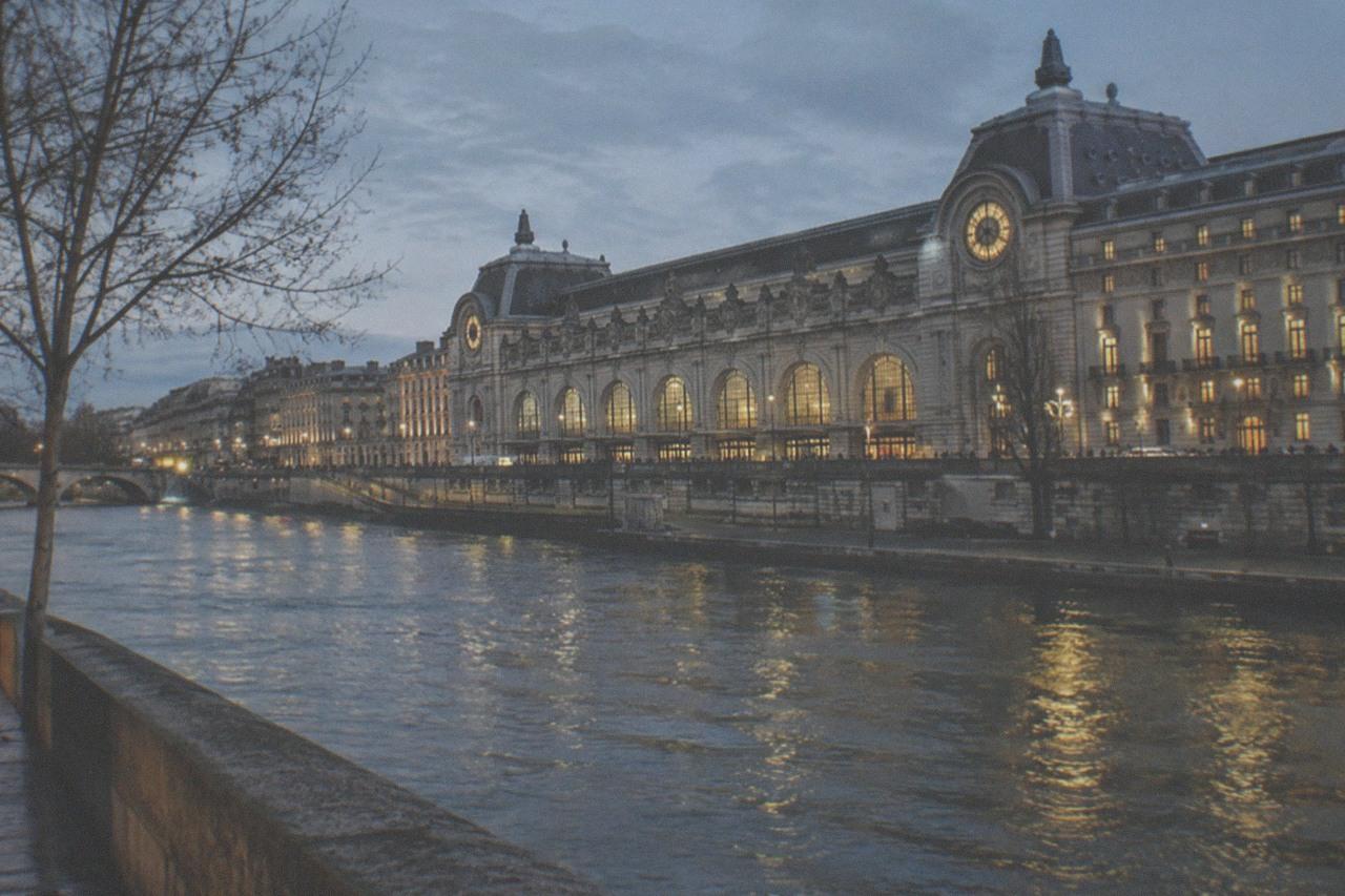 The illuminated facade of the Musée d'Orsay beside the Seine on a blue evening
