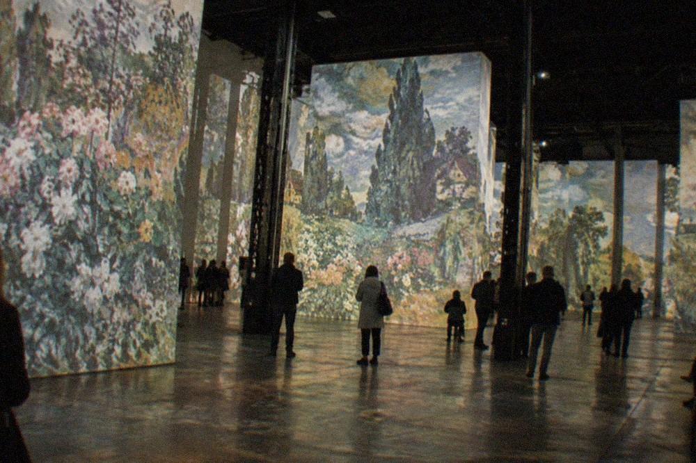 Vivid projected paintings flowing across the tall walls and pillars of a dark industrial hall