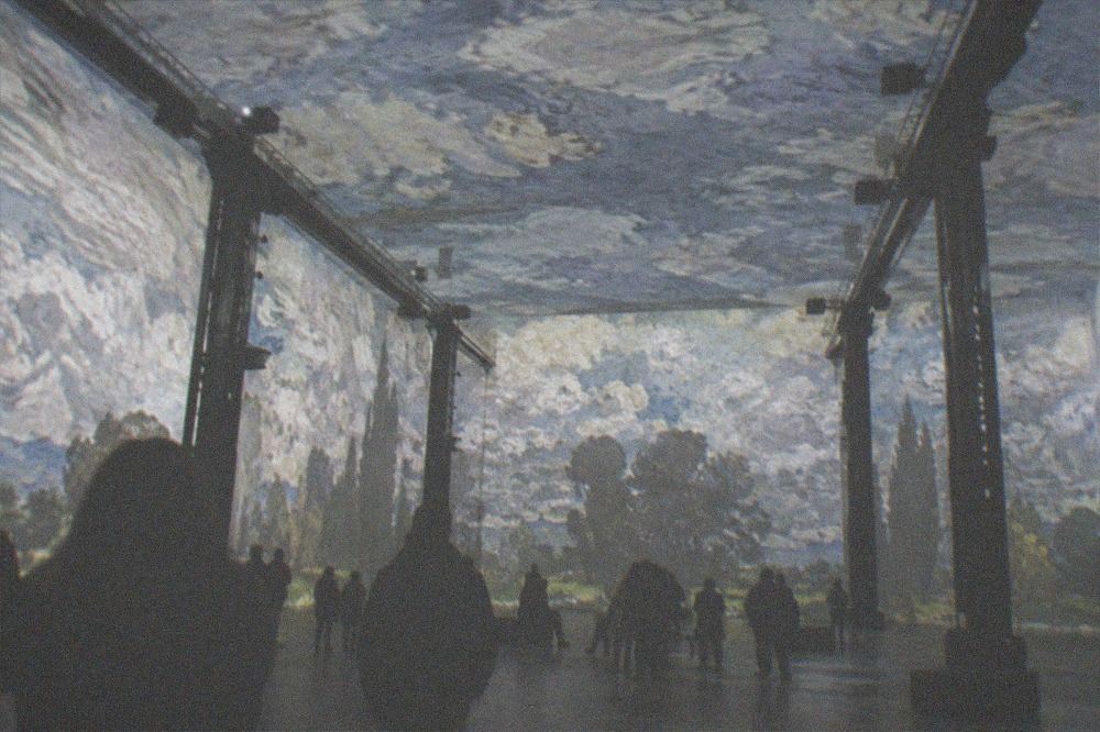 Glowing projection filling the upper walls and ceiling of the industrial venue above silhouetted visitors