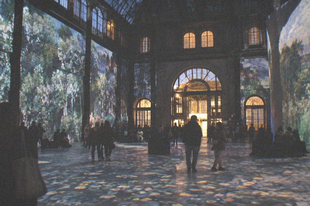 Wide view of the former foundry hall with projected artwork wrapping every wall and visitors spread across the lit floor