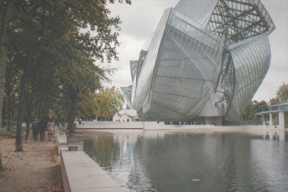 Wide view of a glass sail museum structure across a water basin in a park