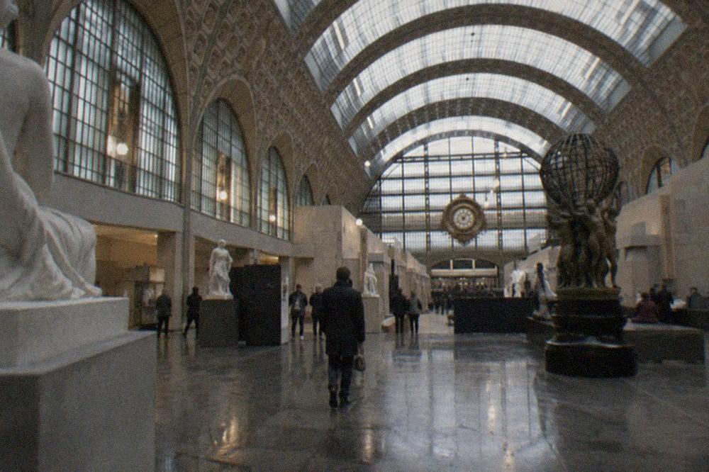 A vast vaulted hall under a curved glass roof, with sculpture on the ground floor of a converted railway station