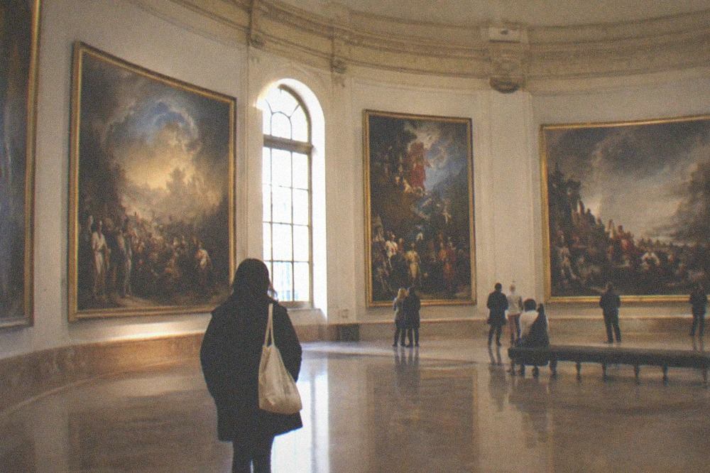 A curved gallery hung with monumental paintings in a softly lit oval room