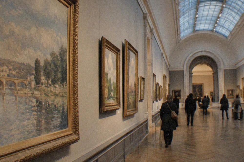 Impressionist paintings hung in rows along a bright gallery with a glass vaulted roof