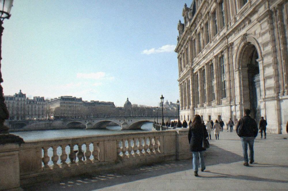 Stone facade of a large museum beside the Seine with a bridge in the background