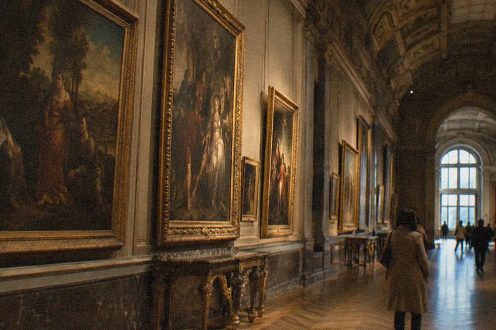 A long gallery of Italian paintings inside the Louvre with frames lit along the walls