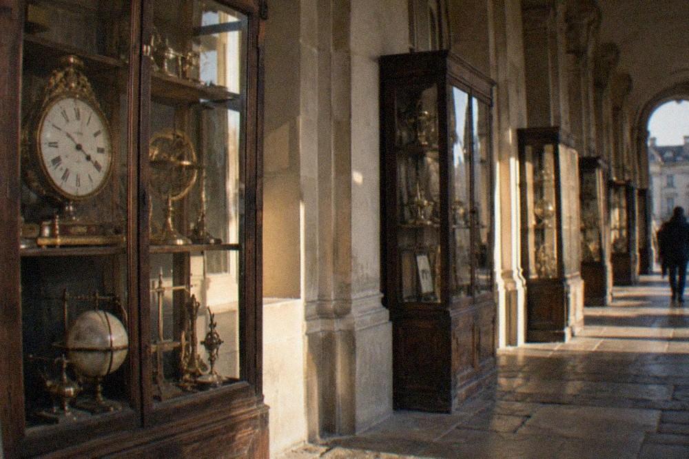 Wooden display cases of old clocks and scientific instruments along a stone gallery