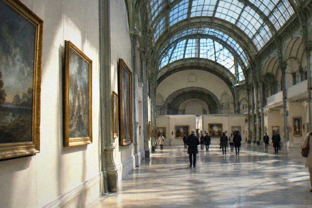 A long gallery hall inside the Grand Palais with paintings hung on pale walls and a vaulted ceiling above