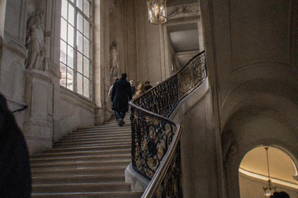 A grand interior staircase in a Paris mansion museum with ornate railing and warm stone walls