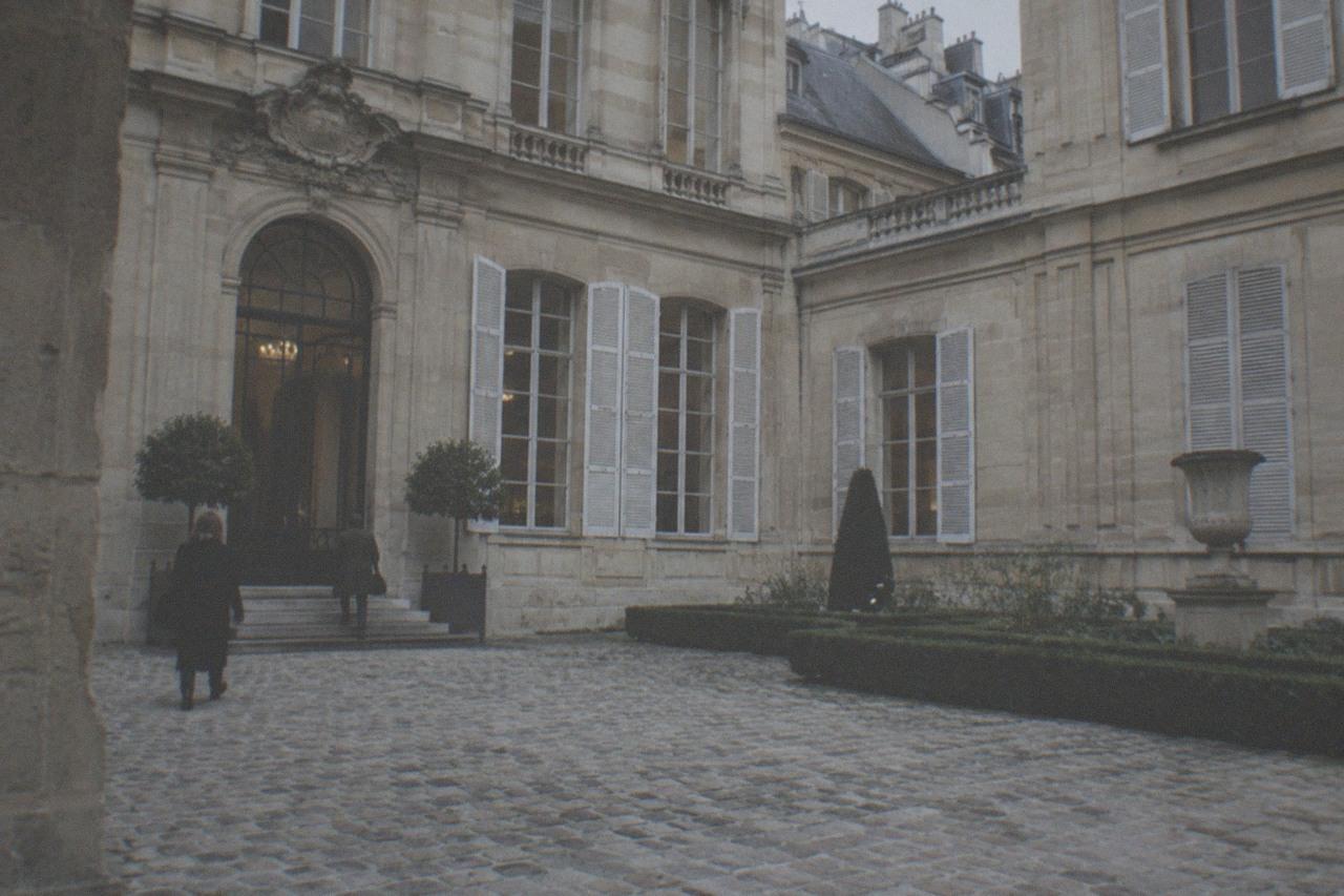 A stone courtyard of a historic Paris mansion with tall shuttered windows and carved detailing above the doorway