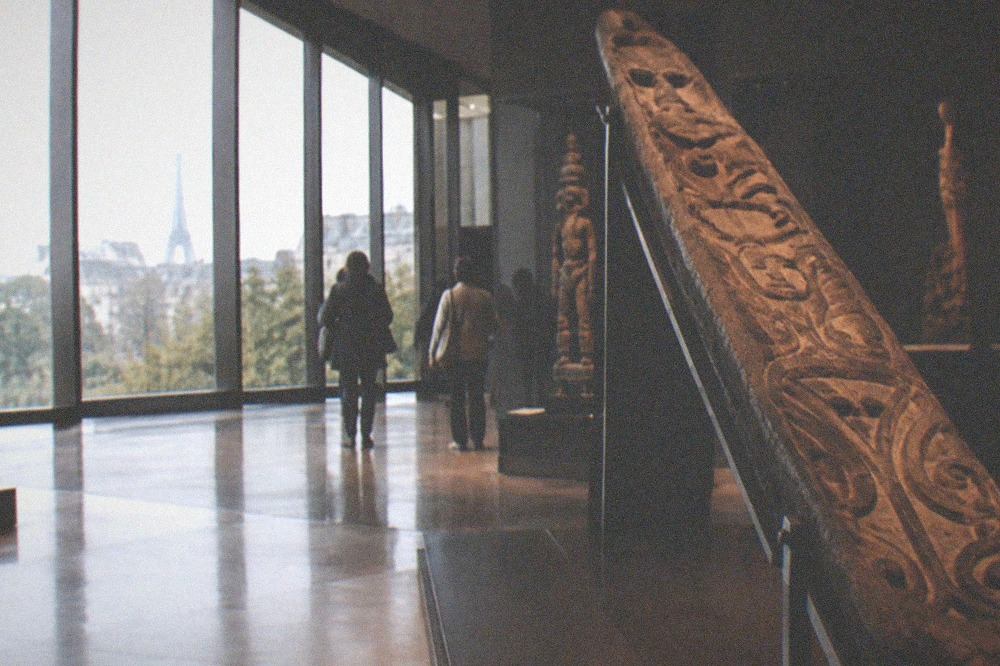 A large carved ceremonial object on an inclined display stand inside a darkened gallery of the Musee du quai Branly