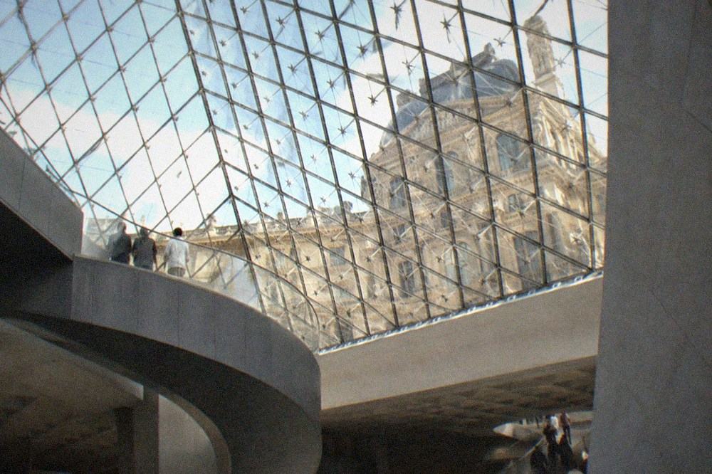 Visitors' view upward through the glass hall toward the metal screens of the museum atrium