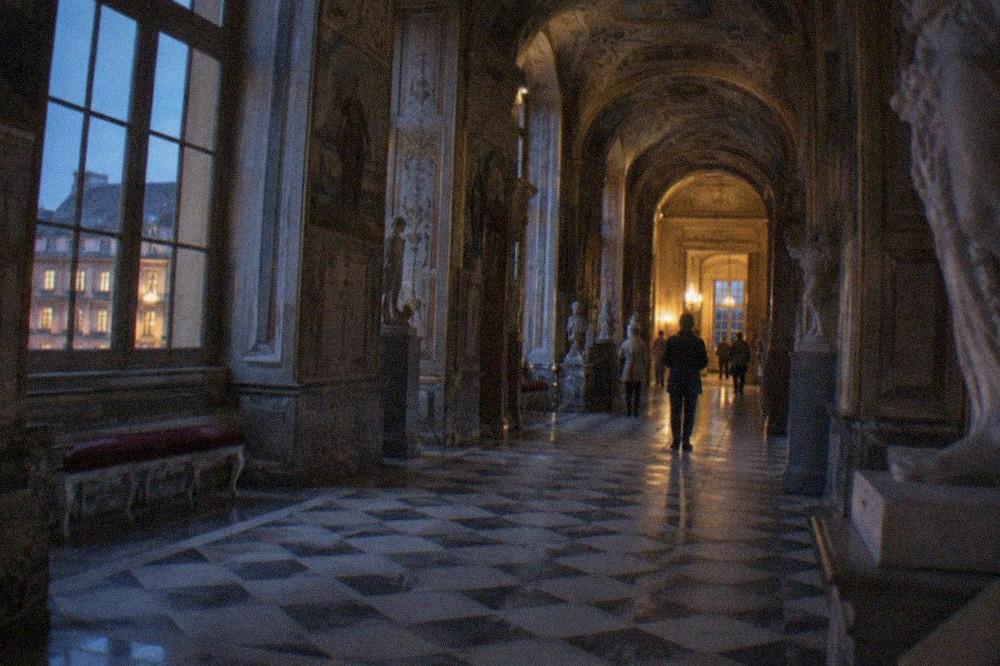 A long frescoed gallery corridor inside a French palace with a patterned floor