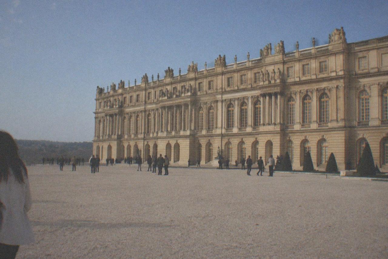A wide gravel forecourt in front of a large French royal palace under a clear sky