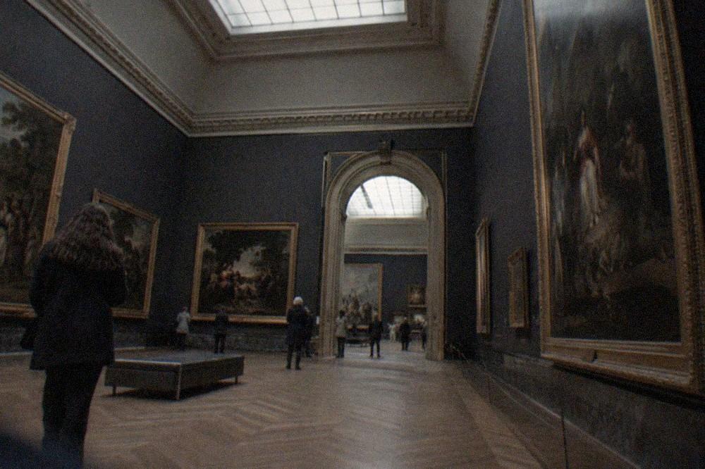A wide museum gallery with dark walls and classical paintings in ornate frames