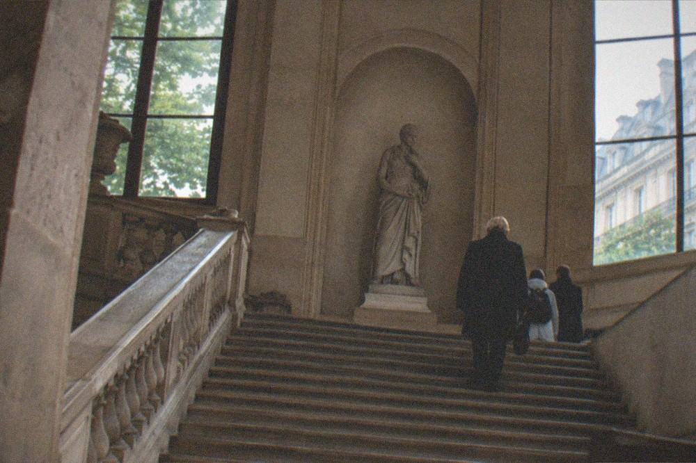 A museum staircase with a sculpture on a landing under a high ceiling