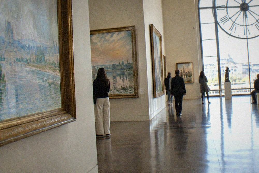Impressionist paintings hung in a bright gallery with a tall clock window