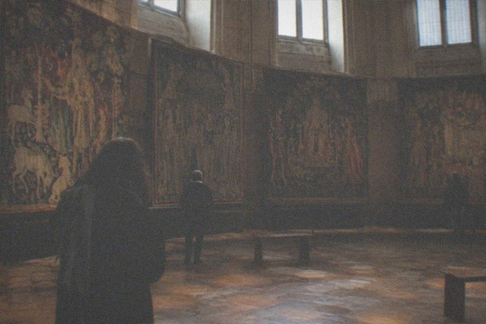 A dim medieval chamber with tall woven hangings displayed in a circle around the room.