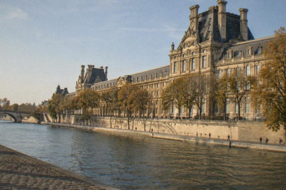 A riverfront view of the Louvre palace stretching along the Seine on a bright afternoon