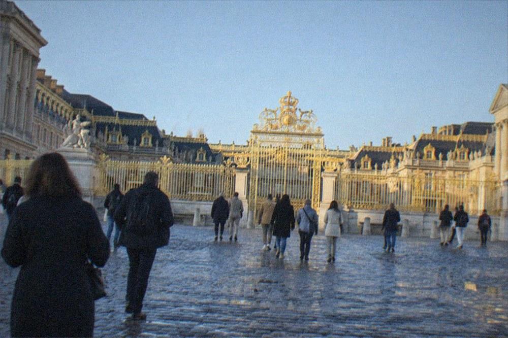 The gilded gate and facade of Versailles seen across the forecourt under a clear sky