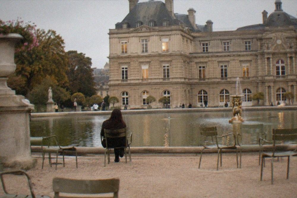 The formal basin and gravel paths of a Paris garden with chairs arranged beside the water