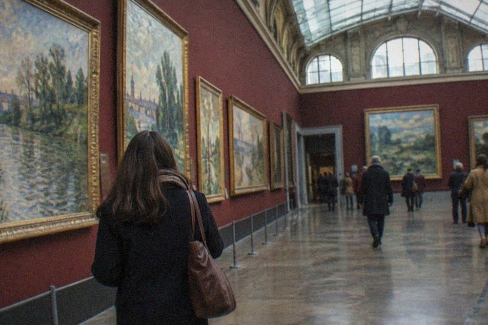 A bright Impressionist painting gallery with large canvases hung on deep burgundy walls under a glass station roof