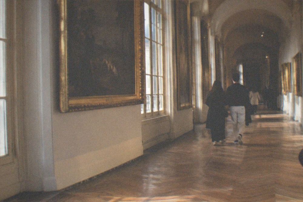 A long gallery corridor with parquet flooring and paintings in gold frames receding into the distance