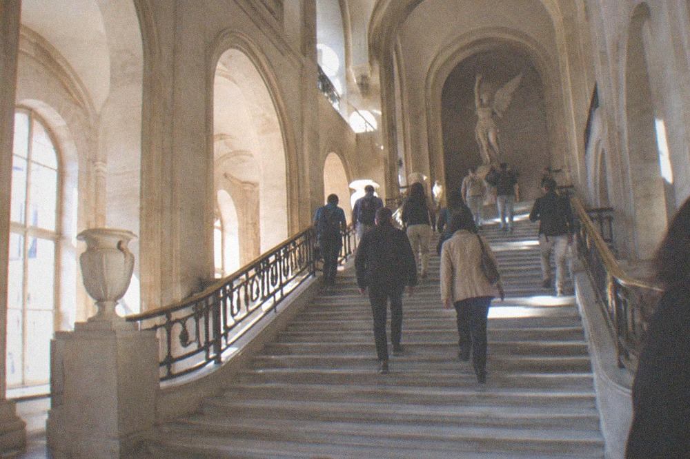 A wide marble staircase inside a museum with visitors moving between floors under high arched ceilings