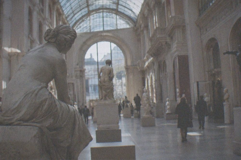A spacious museum hall with a tall arched glass roof and sculptures arranged down the center aisle