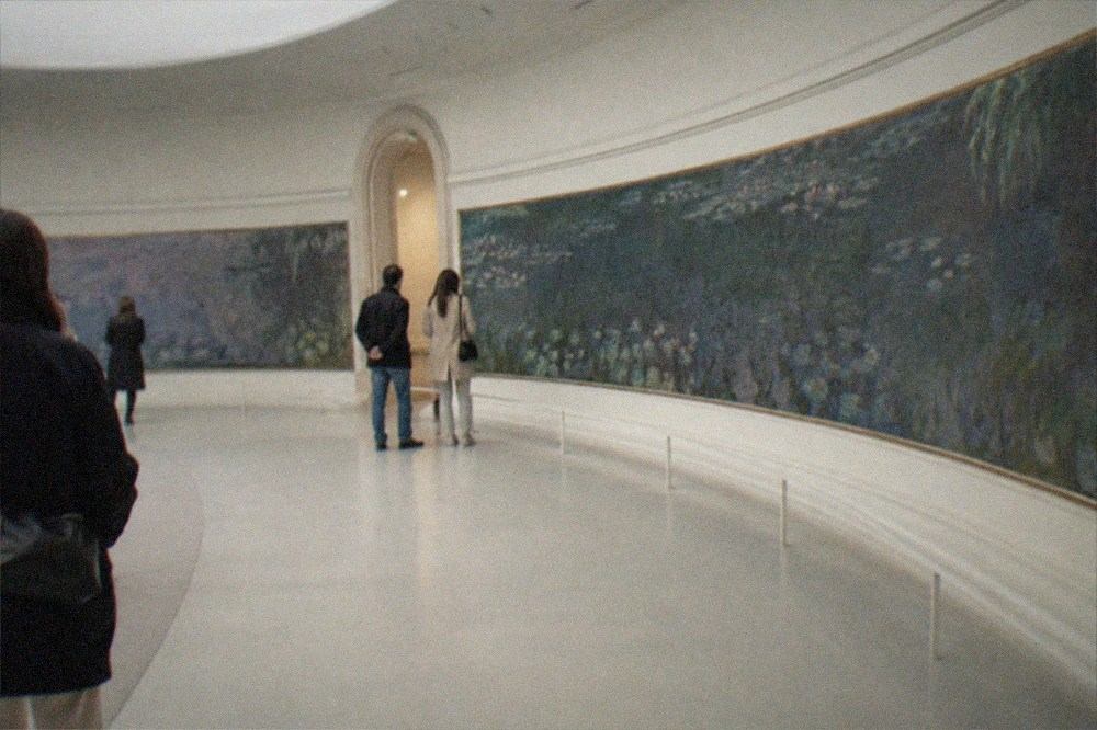 A curved white gallery room with long panoramic water lily paintings wrapped around the oval walls
