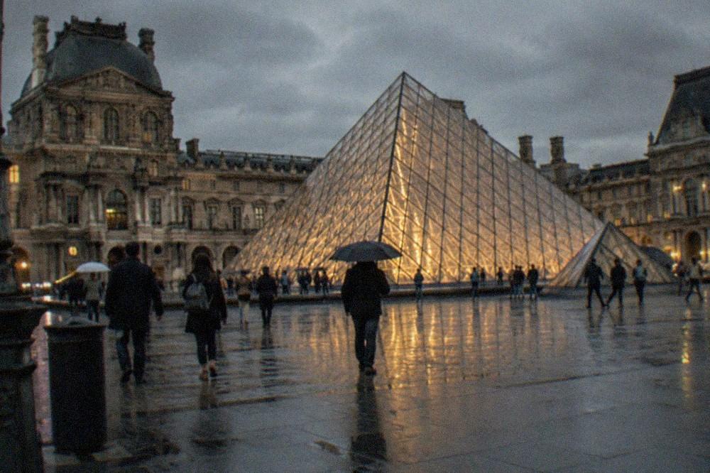 The Louvre pyramid glowing at dusk above the palace courtyard